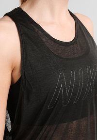Top atlético sin mangas de color negro, fabricado con material ligero, que presenta una capa transparente y un prominente logo de NIKE en un color que contrasta.