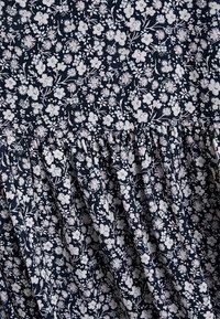 Marineblauwe stof met een bloemenpatroon in wit en roze, met geplooide plooien bij de taille voor textuur en beweging.
