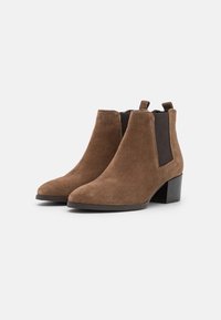 Botas de tobillo de ante marrón con una textura suave, punta afilada, paneles laterales elásticos y un tacón cuadrado. Diseño simple y minimalista.