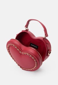 Sac à main en forme de cœur rouge fabriqué en cuir lisse, avec un bord en chaîne dorée, une poignée supérieure et une fermeture éclair. L'intérieur est non doublé.
