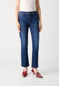 Sinine denim sirge lõikega teksapüksid keskmise kõrgusega vöökoht, millel on ees taskud, vöökaared ja kerge tuhmumine, koos punaste lakipinnaga kontsakingadega.