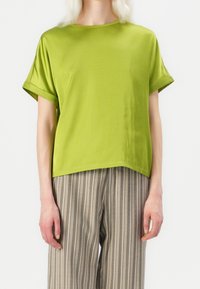 Haut vert à manches courtes avec finition satinée et coupe décontractée, accompagné d'un pantalon gris à larges rayures et jambes larges, présentant un design casual.