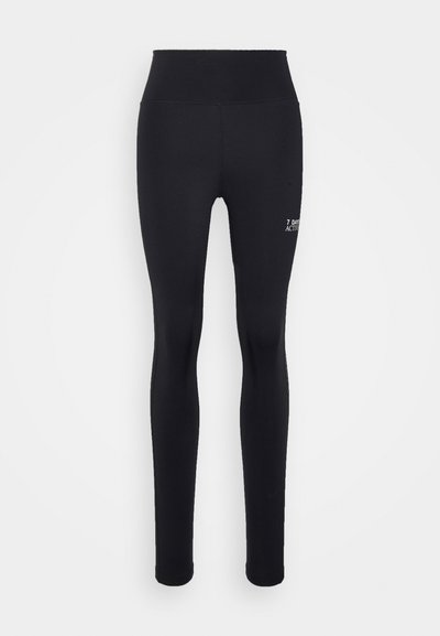 Leggings noirs avec une taille haute, fabriqués en tissu extensible, avec un logo blanc subtil sur la jambe inférieure. Texture lisse et design ajusté.