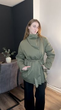 Πράσινο-ελαιόχρωμο φουσκωτό μπουφάν με υπερμεγέθη γιακά, ζώνη στη μέση και δύο πλαϊνές τσέπες. Φοριέται πάνω από μαύρο παντελόνι με φαρδιά πόδια.