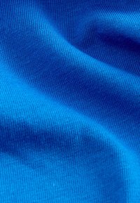 Sinine puuvillane kangas, millel on sile tekstuur ja sooneline muster, featuring folds, mis loovad pehmeid laineid pinnal.