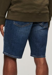 Pantalones cortos de denim en azul oscuro con corte recto. Presentan cinco bolsillos, textura descolorida y costuras en contraste a lo largo de las costuras.