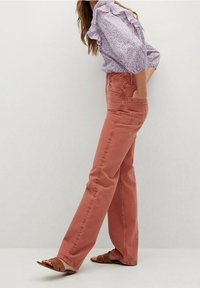 Rostfarbene Jeanshosen mit geradem Bein, ausgestattet mit Fronttaschen und einer hohen Taille. Begleitet von einer rüschigen Blumensbluse.
