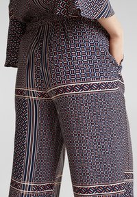 Marinblå mönstrade byxor med geometriska mönster i rött och vitt, med vid siluett och elastisk midja.