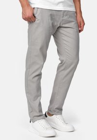 Pantalones de algodón grises con un corte ajustado, que presentan bolsillos laterales y una textura suave, combinados con zapatillas blancas y una camiseta blanca lisa.
