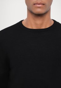 Schwarzer Strickpullover mit glatter Textur, Rundhalsausschnitt und langen Ärmeln, versehen mit einfachen, unauffälligen Stickdetails.