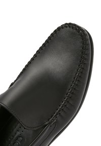 Scarpa nera in pelle scivolata con superficie liscia, punta rotonda e cuciture dettagliate lungo il bordo. Suola piatta, design confortevole.