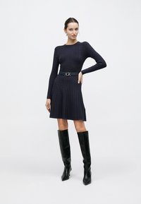 Μπλε ναυτικό πλεκτό φόρεμα με μακριά μανίκια, με εφαρμοστό μπούστο και φαρδύ φούστα. Συνδυασμένο με ψηλές μαύρες δερμάτινες μπότες και ζώνη.