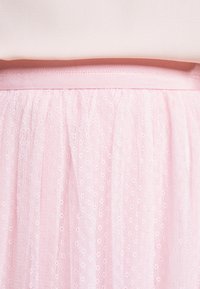 Ljusrosa tullekjol med en rynkad design och ett ribbat elastiskt midjeband. Tyget har ett subtilt prickmönster för textur.