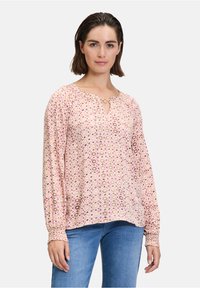 Blusa a maniche lunghe di un rosa chiaro con motivi circolari in viola e beige, dotata di scollatura a chiave e maniche arricciate.