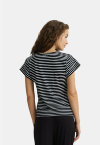 Top a righe bianche e nere a maniche corte con scollatura arrotondata e maniche ripiegate. Presenta un logo sulla parte superiore della schiena. Tessuto dalla consistenza liscia.