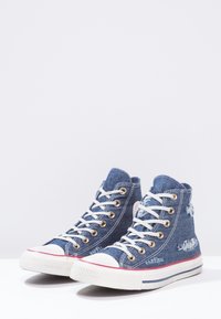 Vysoké tenisky z modrého denimového materiálu s bílými tkaničkami, zlatými očky a gumovou podrážkou, s opotřebovanými akcenty a pruhovaným středovým páskem.