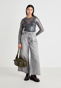 Transparent grey long-sleeve top with leopard print, high-waisted wide-leg grey jeans, and a green crossbody bag with multiple pockets.