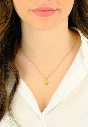 Collier en pendentif en or sur une chaîne fine, mettant en avant un charme sphérique avec des détails délicats, porté sur une chemise blanche à col.