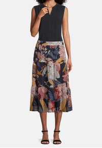 Ärmlös svart topp med V-urringning, kombinerad med en blommig lagerkjol som har flerfärgade blommor och lövmönster på en mörk bakgrund.