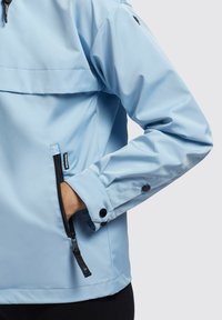 Veste étanche bleu clair avec un col haut, poche latérale zippée et poignets à boutons. Tissu lisse avec une coupe décontractée.