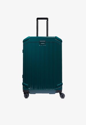 Maleta rígida de color verde azulado oscuro con ranuras verticales, asa negra retráctil y cuatro ruedas para facilitar su movilidad. Cuenta con una placa de nombre personalizable.