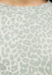 Απαλό ύφασμα σε ανοιχτό πράσινο με διακριτικό μοτίβο λεοπάρ. Στρογγυλεμένος λαιμός με υφή και ριμπ τελείωμα κατά μήκος των άκρων.