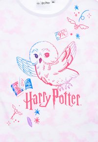Camiseta blanca con efecto de tie-dye rosa, que presenta un búho de dibujos animados, texto de "Harry Potter" y coloridos iconos mágicos en azul y rosa.