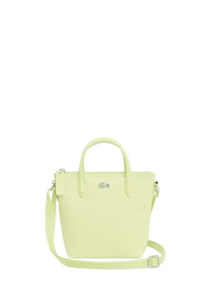 Pequeña bolsa tote de color verde claro con dos asas, correa ajustable para el hombro, cierre con cremallera y logo de cocodrilo de Lacoste en el frente.