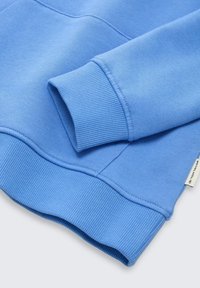 Felpa azzurro chiaro con polsini e orlo a costine, caratterizzata da una texture morbida e cuciture precise. Un piccolo etichetta con il marchio è visibile sul lato.