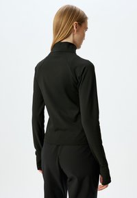 Top negro de manga larga con cuello alto y silueta ajustada, hecho de tela elástica; cuenta con mangas raglán y agujeros para los pulgares.