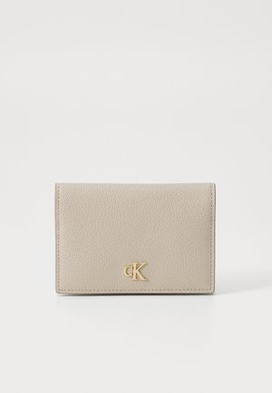 Portefeuille en cuir beige avec une surface texturée et un logo "CK" doré. Forme rectangulaire compacte, avec des bords cousus et un design à rabat.