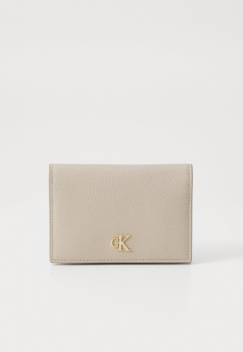 Beige leather wallet featuring textured surface and gold "CK" logo. Compact rectangular shape, with stitched edges and fold-over design.