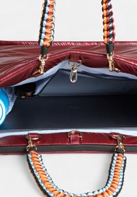 Glanzende bordeauxkleurige synthetische tas met gevlochten multikleurige banden. Het interieur heeft een lichtblauwe voering, een vak voor een waterfles en cliphardware.