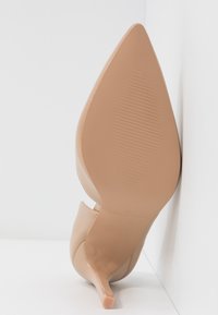 Chaussure à talon haut nude avec un bout pointu et un talon stiletto fin. Matière synthétique lisse, avec une semelle texturée et un design ajouré.