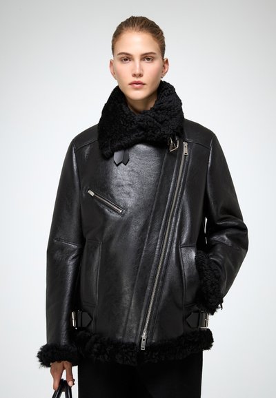 Sort læderjakke med en fluffy sort krave og kant, med diagonale lynlåse og en struktureret design. Blød tekstur, skræddersyet pasform.