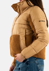 Beige isolerad jacka med en mjuk, lurvig nederdel och slät övre del; med dragkedjefickor och hög krage för extra värme.