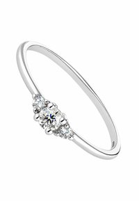 Anillo de metal plateado con un diamante redondo central y dos diamantes redondos más pequeños a cada lado; acabado elegante y pulido.
