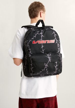 Černý batoh s šedým vzorem připomínajícím trny, s červeným logem „Vans“. Má polstrované popruhy a přední kapsu na uložení věcí.