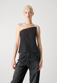 Top noir à une épaule avec un design structuré, présentant des coutures verticales et une silhouette ajustée. Associé à un jean en denim noir ample.