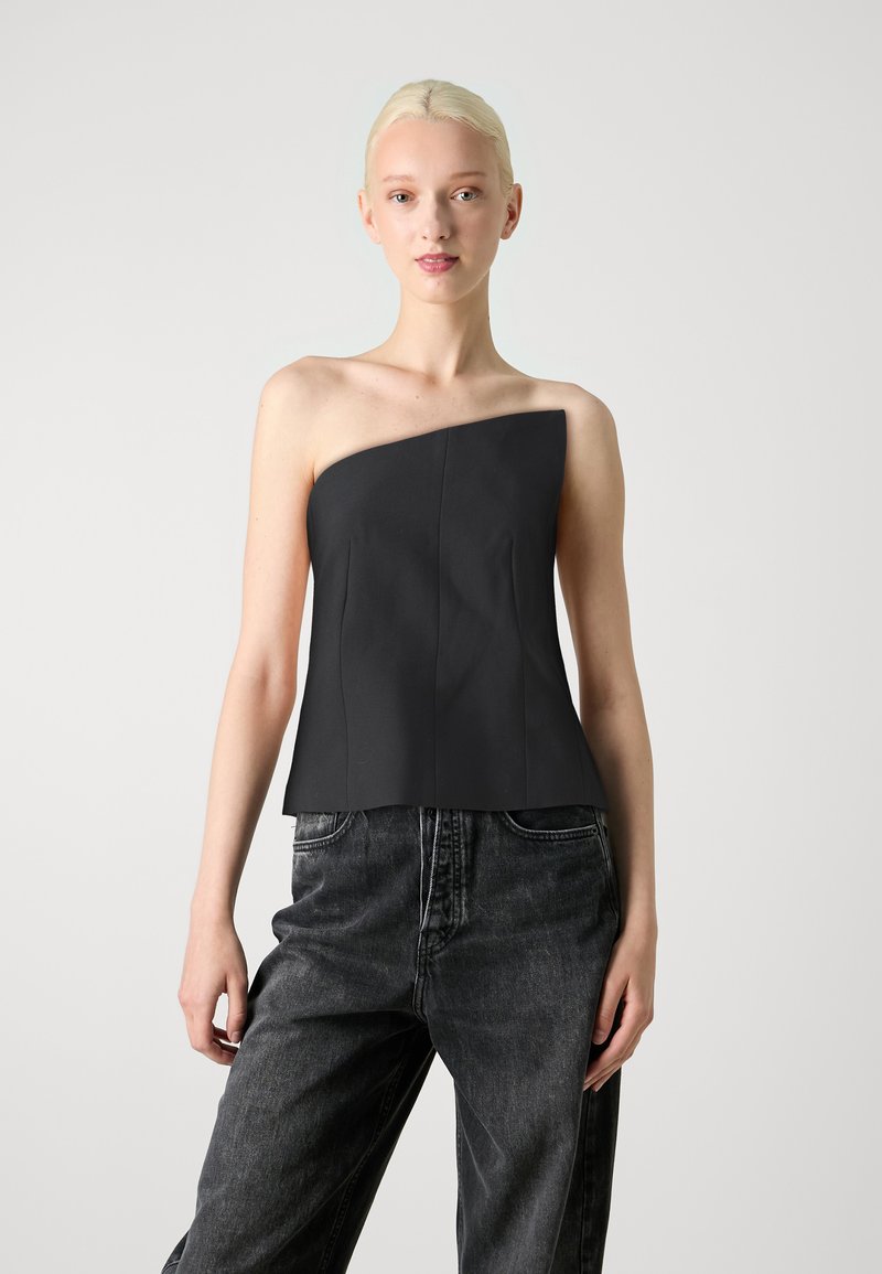 Top noir à une épaule avec un design structuré, présentant des coutures verticales et une silhouette ajustée. Associé à un jean en denim noir ample.