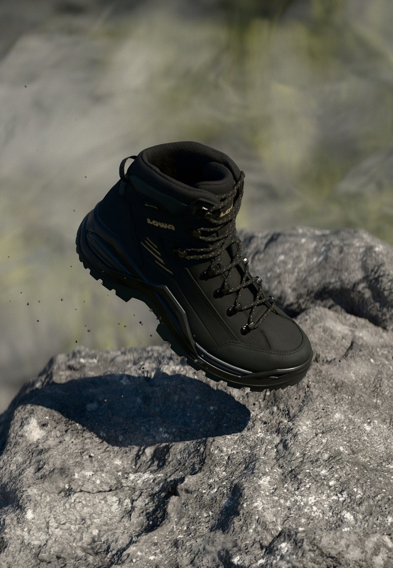 Une botte de randonnée noire avec des lacets étiquetés "LOWA" flotte au-dessus d'une surface rocheuse grise et rugueuse en plein air.