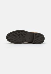 Brown leather shoe with a textured black rubber sole, featuring a herringbone pattern for grip. Brand logo visible on the sole.