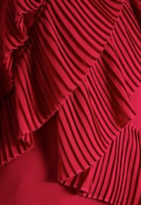 Červená skládací tkanina s několika vrstvami, která má texturovaný povrch. Sklady jsou symetrické a vytvářejí plynulý design.