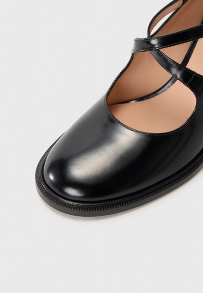 Chaussure en cuir noir avec des brides croisées, bout arrondi et finition lisse. Présente un subtil détail en relief sur la semelle.