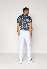 Kortermet skjorte med et svart-hvitt grafisk trykk, kombinert med hvite bukser, fremhevet av en glattere tekstur og slim fit.
