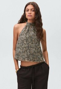 Halter neck crop top in dark green with a floral pattern in beige and cream. Soft fabric with a loose, relaxed fit.