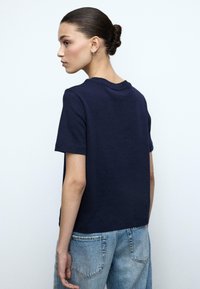 Donkerblauw katoenen T-shirt met korte mouwen en een ronde hals, gedragen met lichtgewassen denim jeans. Eenvoudige en ontspannen pasvorm.