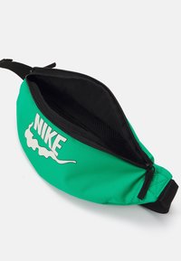 Grön nylon midjeväska med svart dragkedja, med en vit Nike-logotyp. Inuti har den svart foder och en meshficka för organisation.