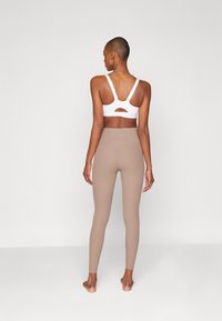 Soutien-gorge de sport blanc avec détail découpé et bretelles ajustables, associé à un legging taille haute beige avec une texture lisse et une coupe ajustée.
