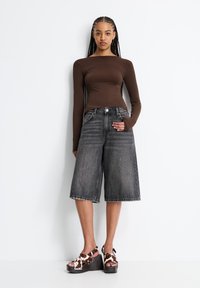 Top marrone a maniche lunghe, culotte in denim grigio a vita alta, sandali con zeppa marroni e bianchi a motivo e tacco spesso.